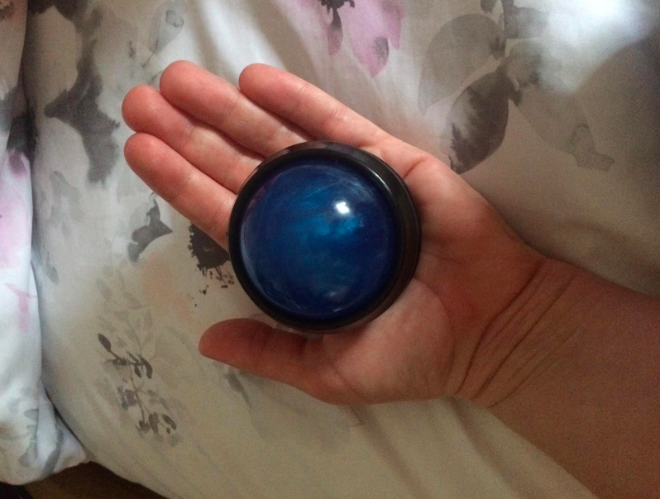 A blue massage ball held in a hand resting on bed sheets 
