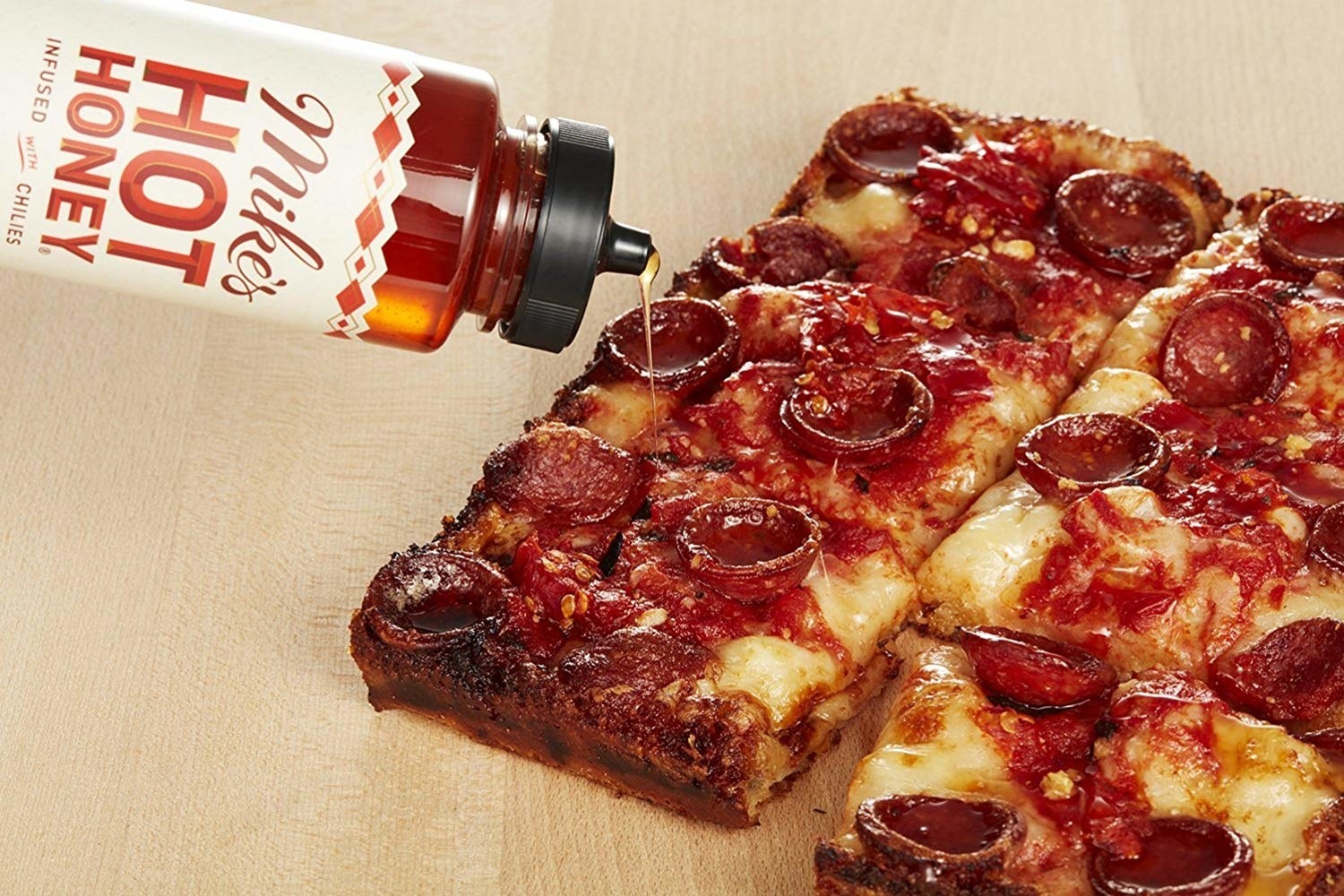 Container of honey oozing onto square pepperoni pizza 