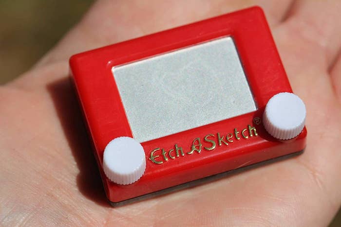 a hand holding a small red Etch A Sketch