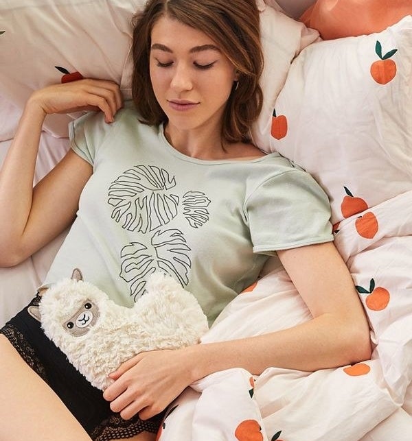 A person laying down in bed with the llama cooling/heating pad on their stomach