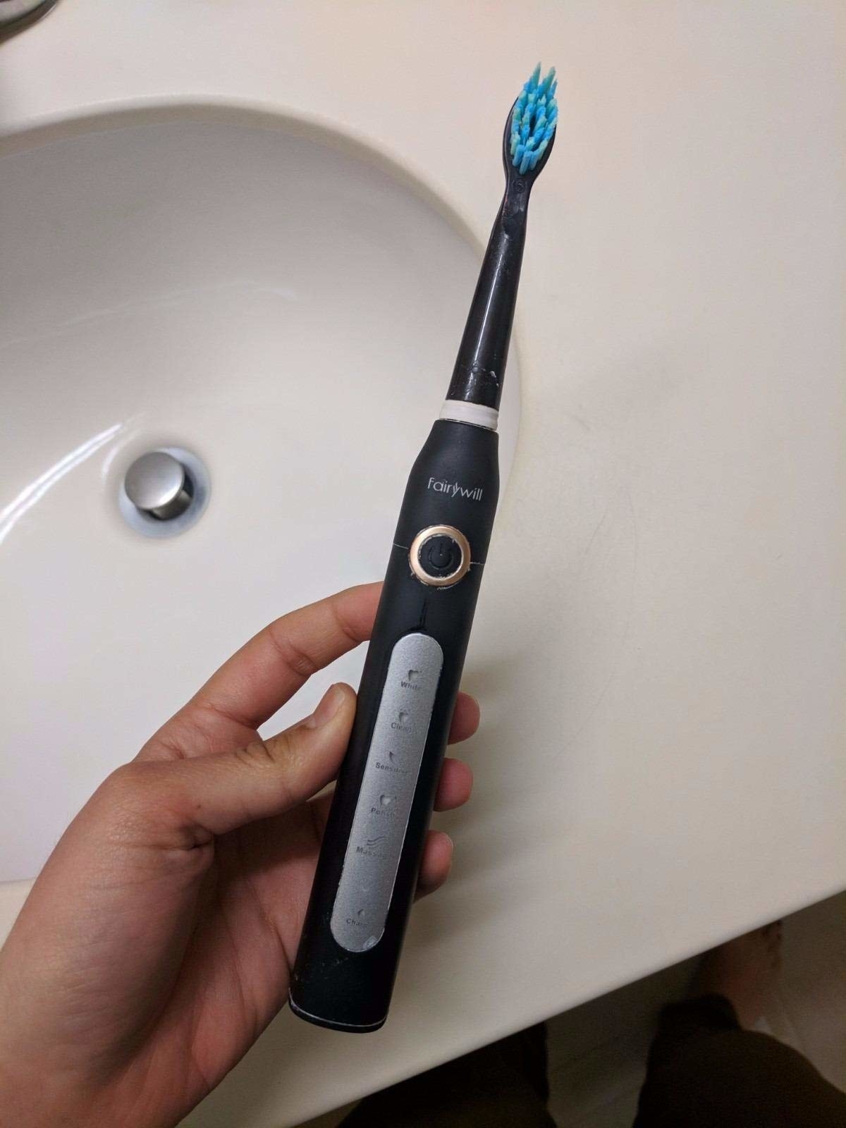Reviewer holding the electric toothbrush, showing the different settings