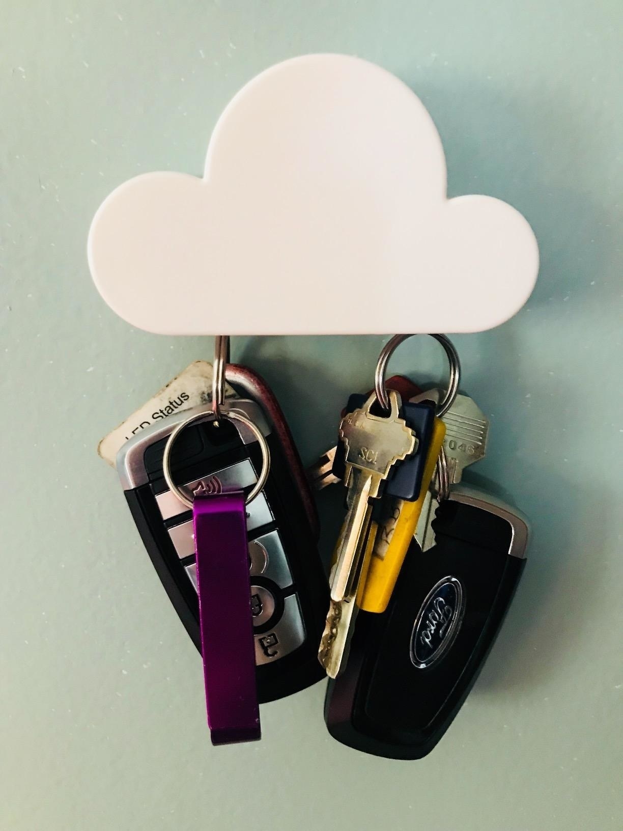 A minimalist cloud magnet tacked to a wall holding two sets of car keys 