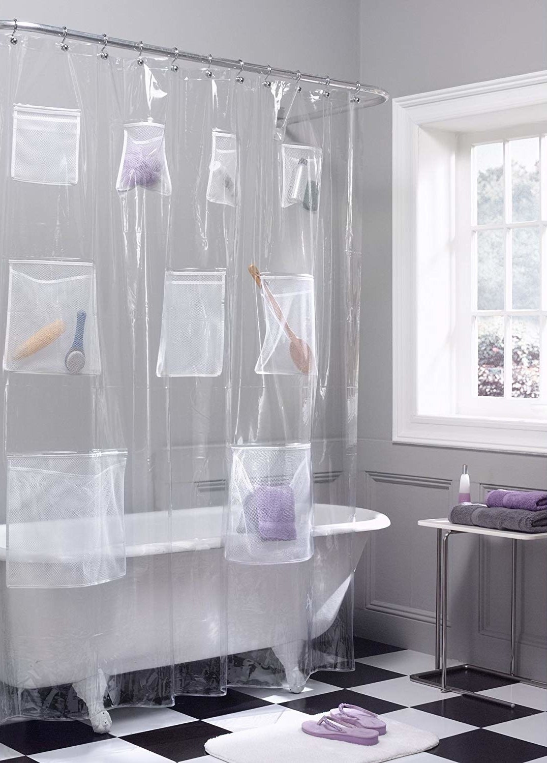 clear shower curtain with mesh pockets filled with towel, shampoo, brush, and other items