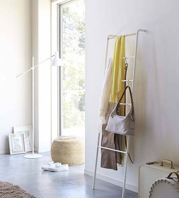 The white ladder holding blankets, a bag, a belt, and more