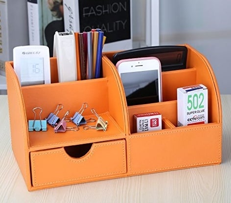 The orange organizer, which has a shelf, two small compartments, three large compartments, and a little drawer. It&#x27;s holding things like pencils, a calculator, phone, and binder clips
