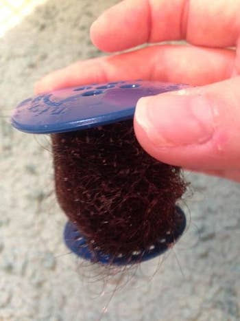 Reviewer's blue drain stopper-shaped tubshroom with wet hair wrapped all around it 