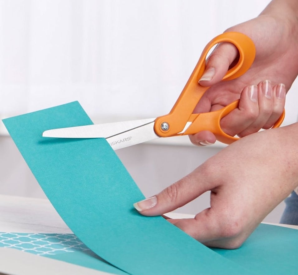 Hands using the orange scissors to cut cardstock