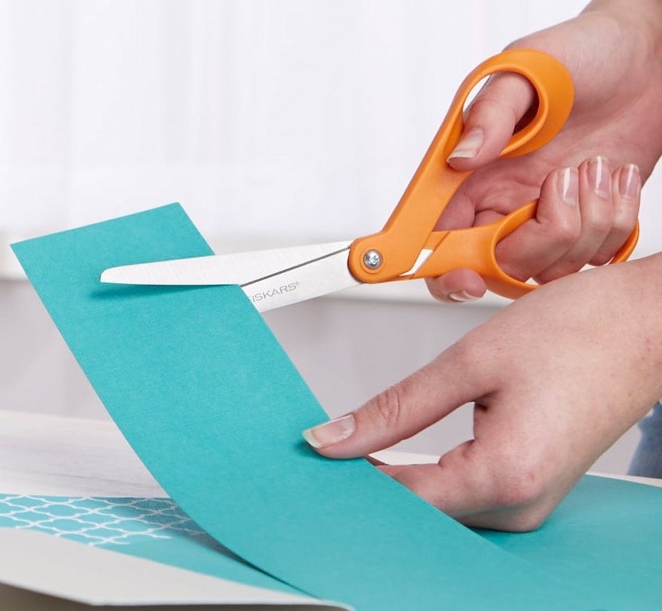 Hands using the orange scissors to cut cardstock