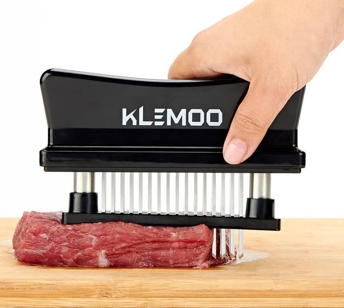 A model holding a device with spikes that are being pressed into a slab of meat