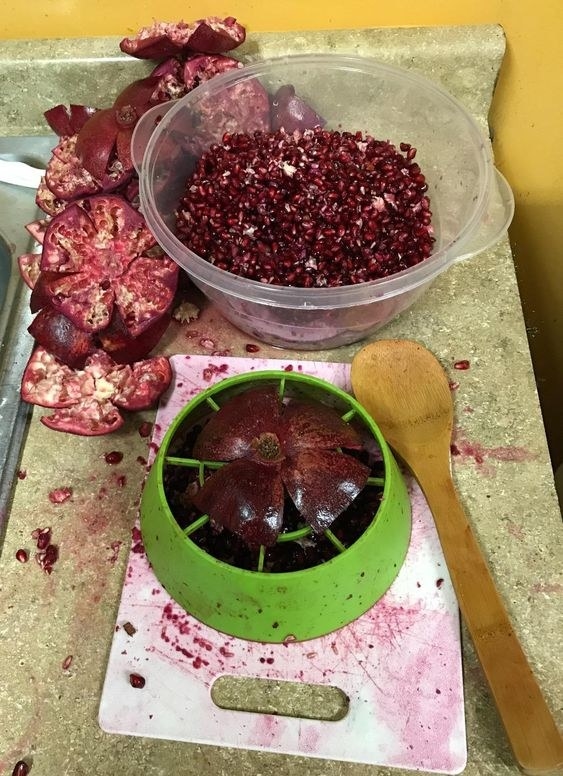 A reviewer&#x27;s bowl of pomegranate seeds, plus the empty husk of pomegranate showing how effective the round plastic tool is