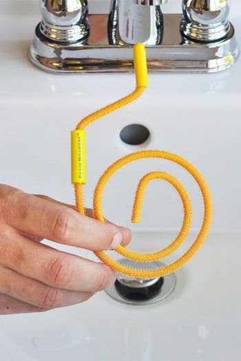 person holding up the coiled hair remover in front of a sink