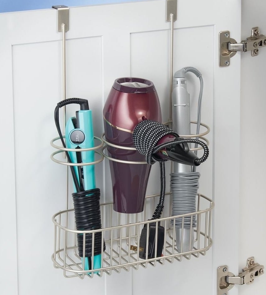 The organizer hanging over the inside of a cabinet door. It has three circular compartments, shown holding flat and curling irons and a hair dryer
