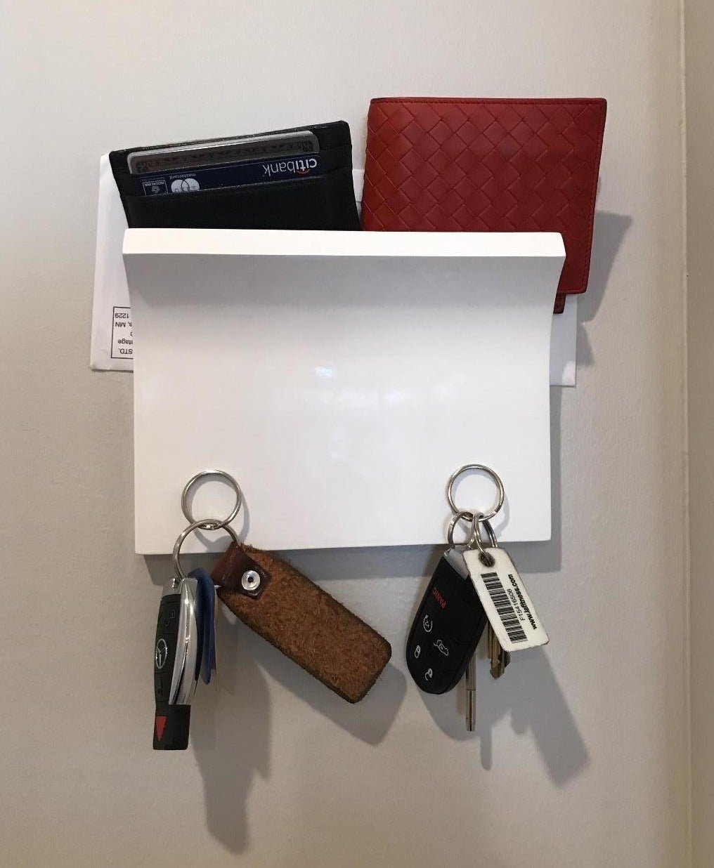 the white organizer mounted to the wall holding some mail two wallets and two sets of keys