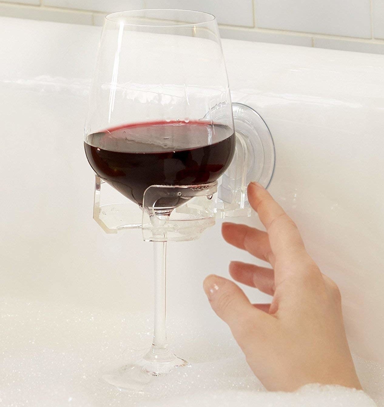 hand reaching for wine glass in clear suction cup bathtub holder