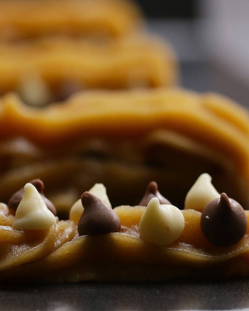 12人分材料：バター(1cm角) 125g黒砂糖 85g水 230ml塩 小さじ1薄力粉 250g卵 3個バニラエクストラクト 大さじ1ラム酒 大さじ1チョコレートチップ(ブラック、ホワイト) 適量揚げ油 適量グラニュー糖 100gシナモン 大さじ1作り方：1.揚げ油を190℃に余熱しておく。2.鍋にバター、黒砂糖、水、塩を加えて火にかける。3.沸騰したら中火にし、薄力粉を加えて絶えず木べらでかき混ぜる。ひとまとめになったら火から下ろして5分ほど冷ます。4.(3)に卵を1個ずつ割り入れてその都度かき混ぜる。バニラエクストラクト、ラム酒を加えてよく混ぜ、口金の付いた絞り袋に移す。5.クッキングシートを敷いた天板に(3)を5cmほど絞り出し、チョコレートチップを乗せる。さらに上から生地を絞る。6.(5)を冷凍庫に入れて20分冷やし固める。7.揚げ油に(6)を入れ、きつね色になるまで2-3分揚げ、油をしっかり切ってバットに上げる。8.ボウルにグラニュー糖、シナモンを加えて混ぜ合わせ、(7)にまぶしたら、完成！