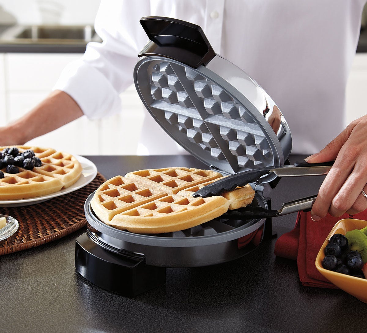 Someone removing a cooked waffle from the silver waffle maker