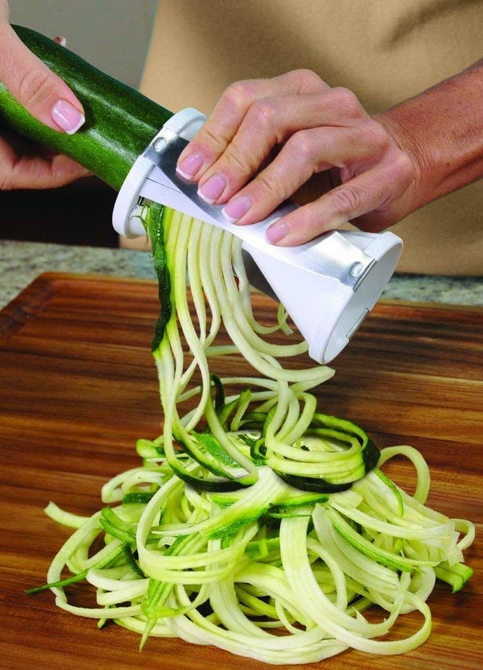 A hand using the spiralizer, which is similar to a large pencil sharpener, to make zucchini noodles 
