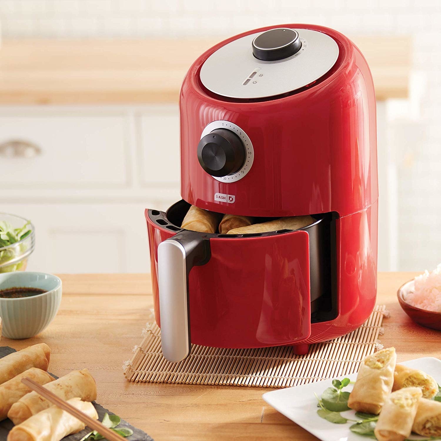 The air fryer in red, featuring an analog timer, round temperature dial, and convenient handle for removing the basket 