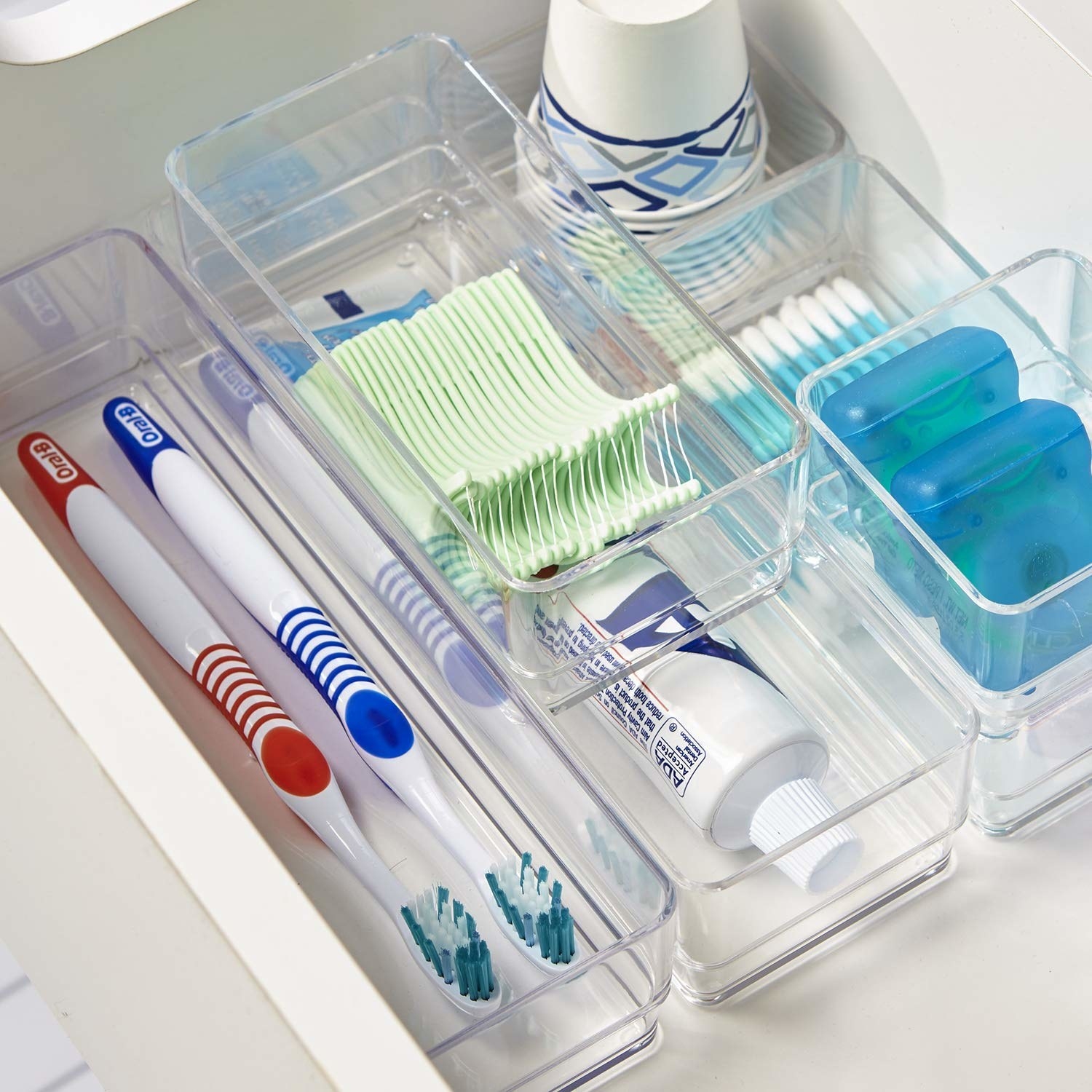 The organizers in a drawer holding toothbrushes, toothpaste, floss, cotton swabs, and cups