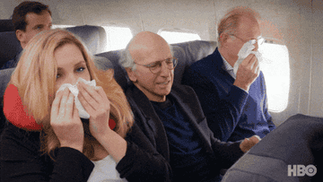 A gif of Larry David squished in a middle seat next to a bunch of sick travelers