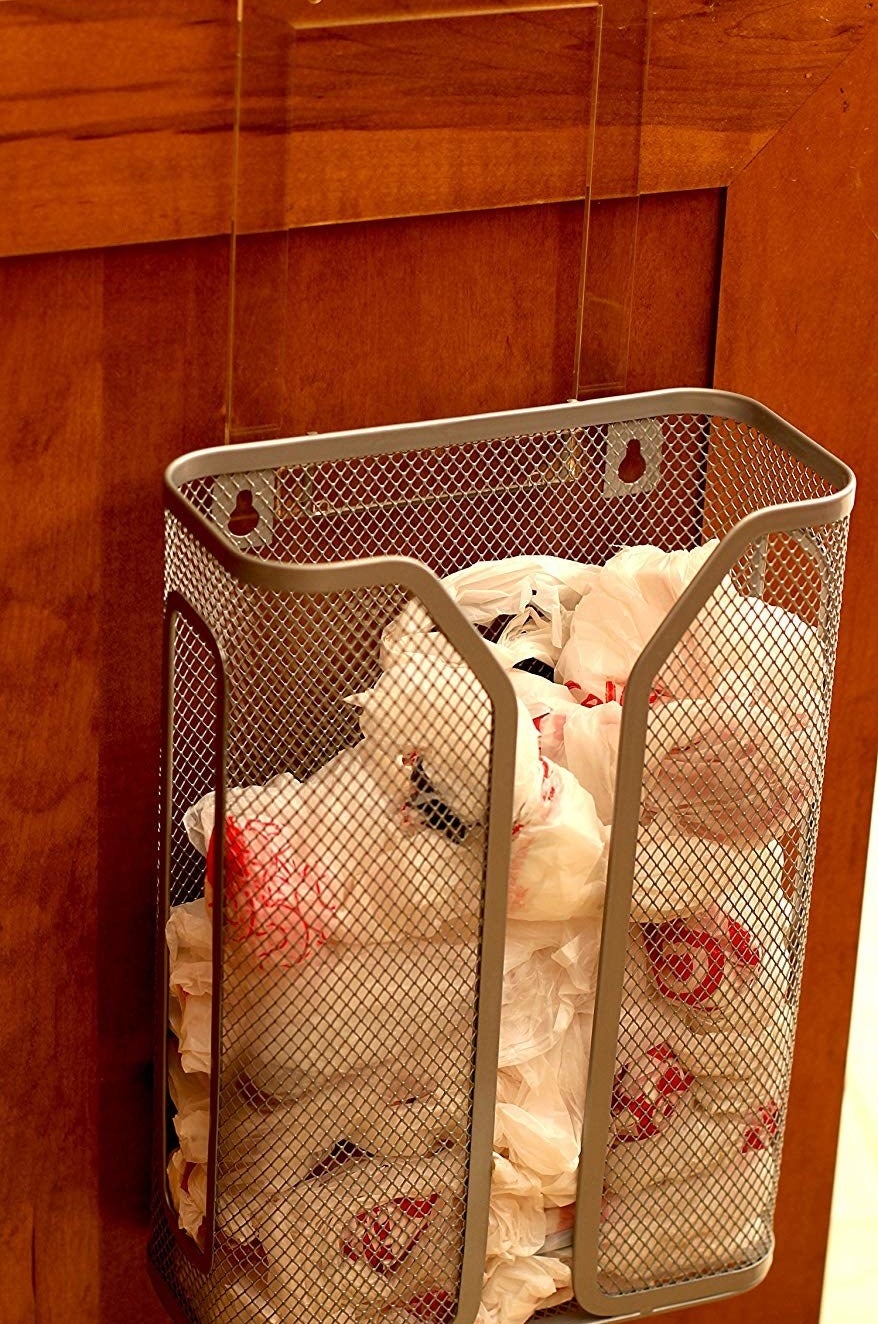 The metal mesh bag holder attached to the inside of a cabinet with a number of plastic bags inside