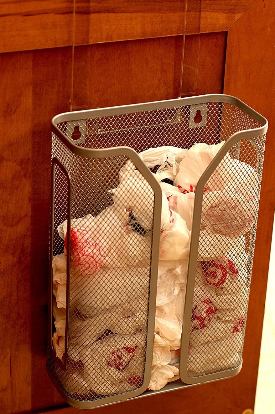 The metal mesh bag holder attached to the inside of a cabinet with a number of plastic bags inside