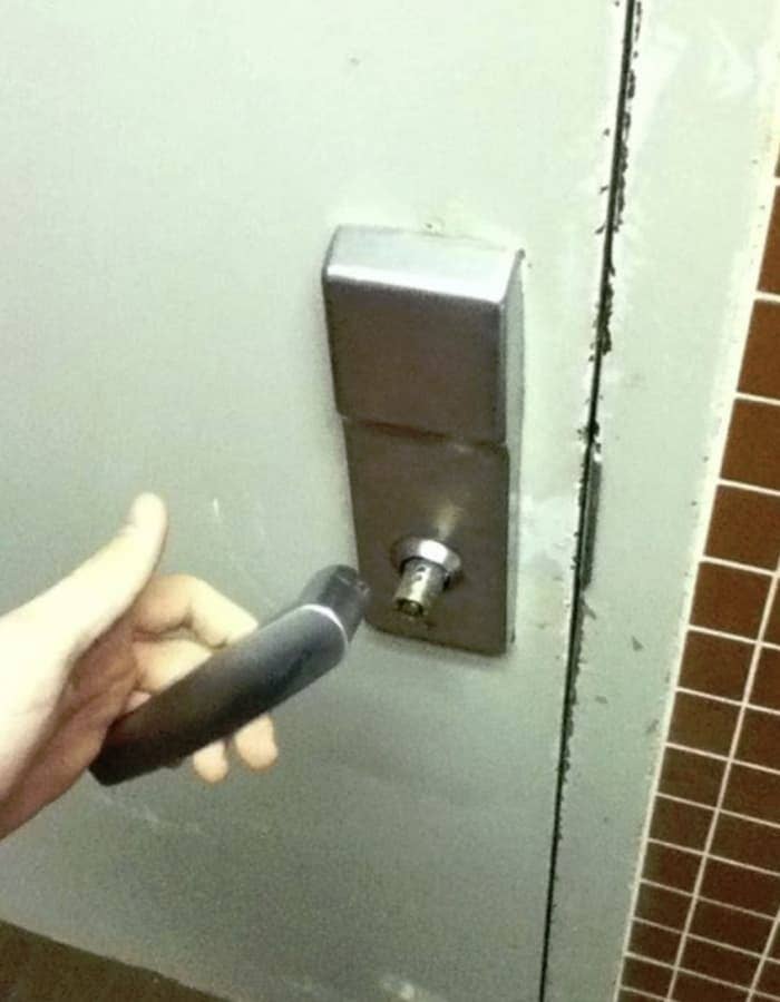 A person holds a broken door handle detached from the door lock. The lock mechanism is exposed