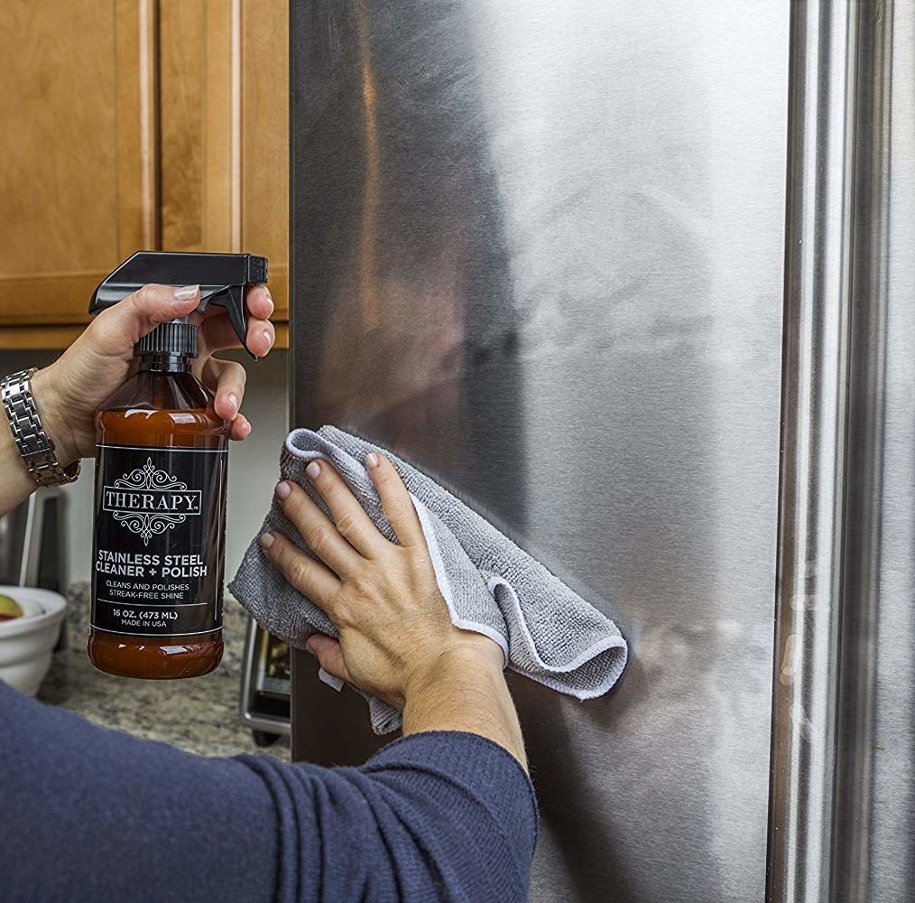 Hand wiping a fridge door after applying the cleaner