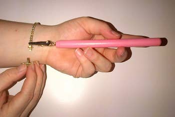 hand using the tool (a pencil-length handle with a clip on the end) in pink