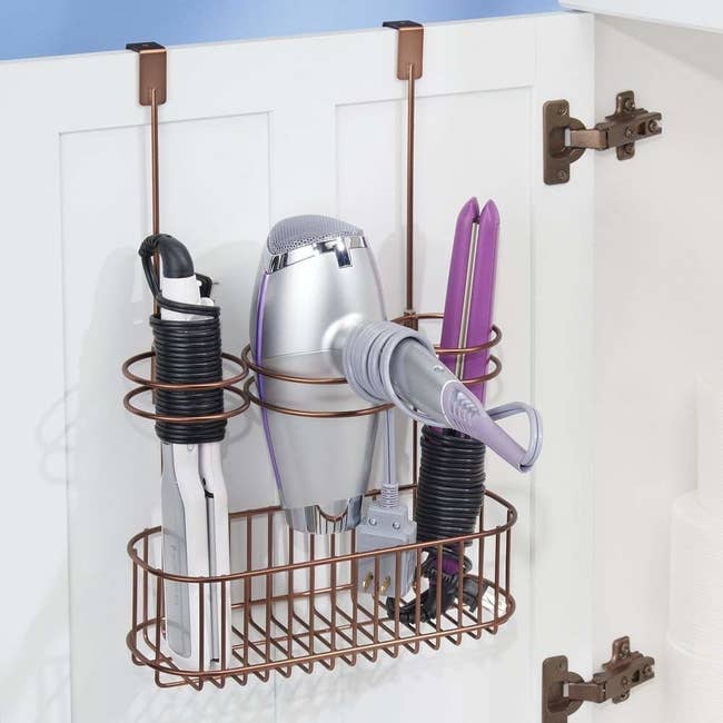 The storage rack in a brass color holding a hair dryer, flat iron, and curling iron