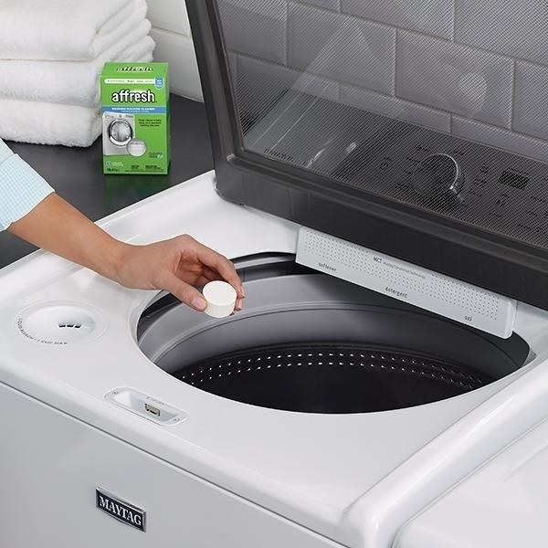 models hand dropping 1/4c-ish size tablet into washer