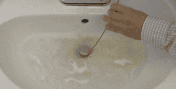 Gif of hands pushing snake down drain, twisting, then gradually pulling it up, bringing a wad of wet hair with it
