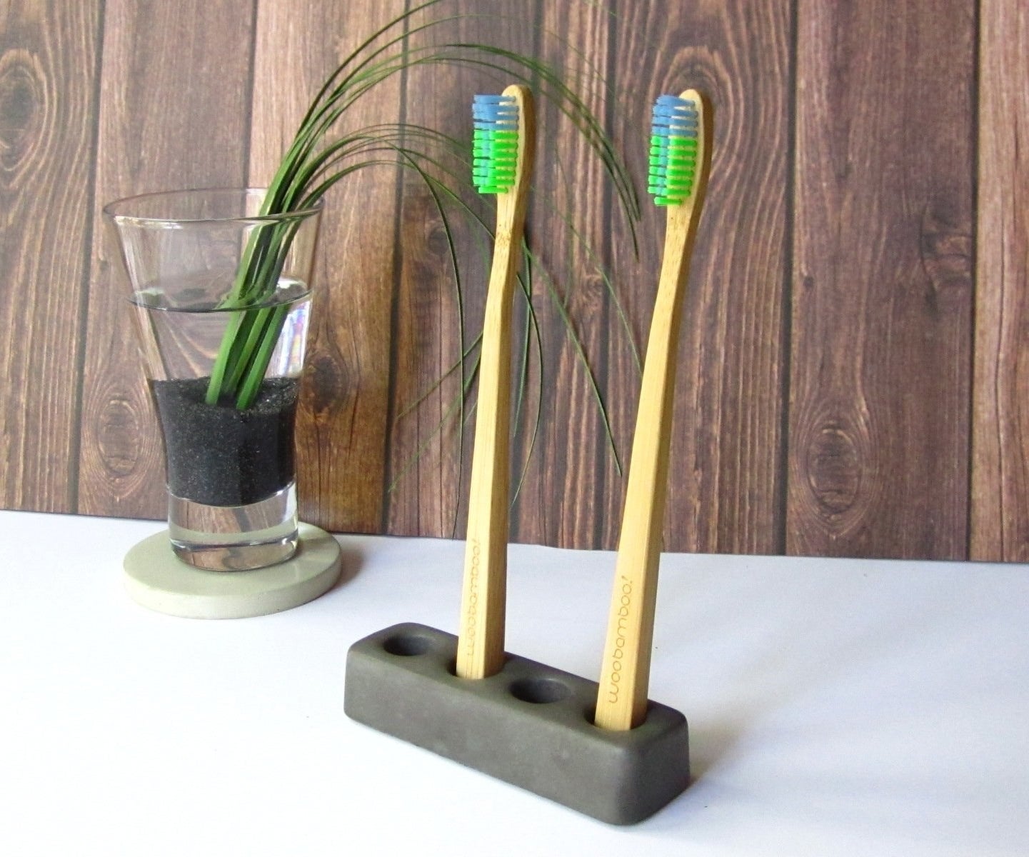 Cement toothbrush holder with room for four brushes holds two wooden toothbrushes on a bathroom countertop.