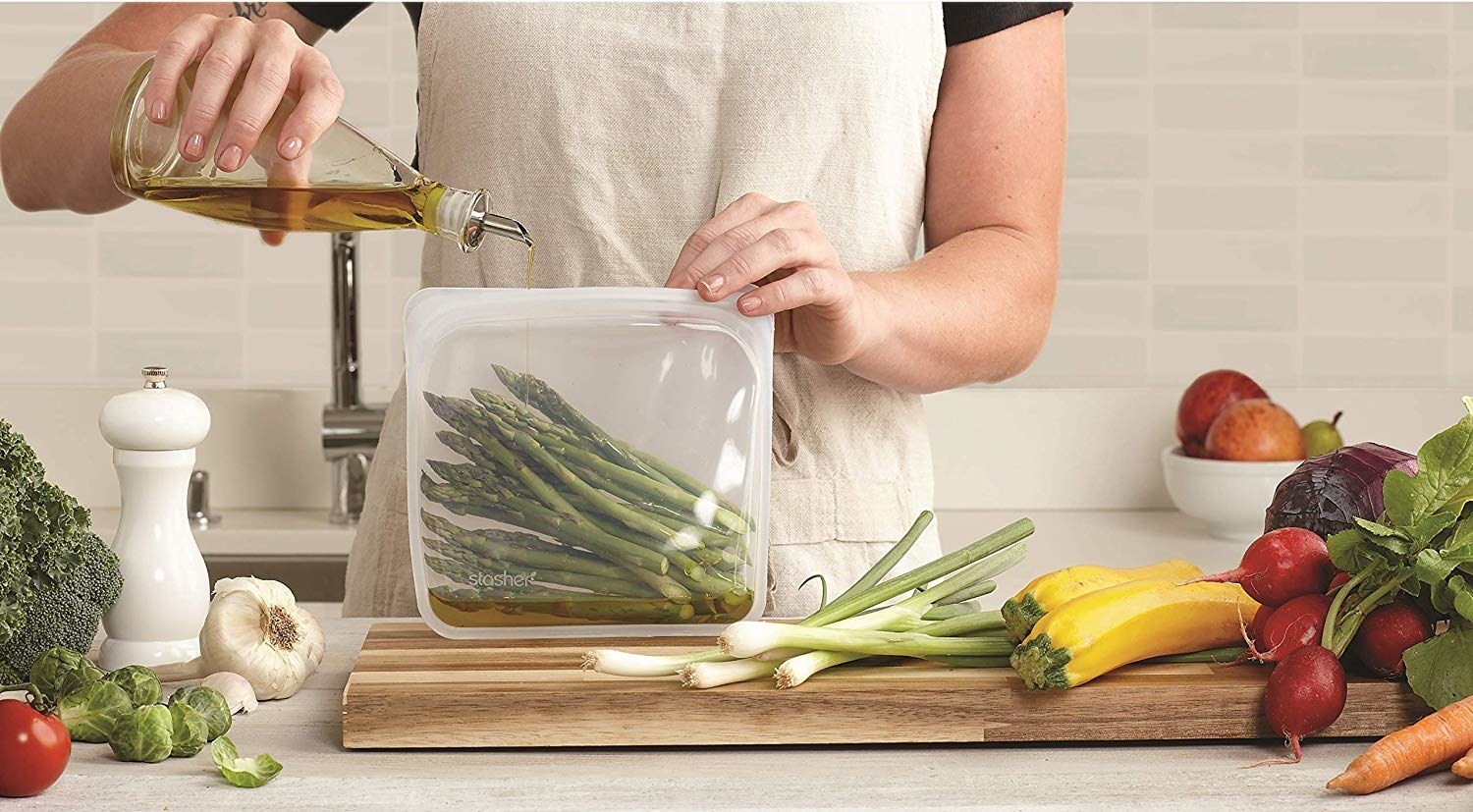 a person pouring olive oil into asparagus that are in the reusable bag 