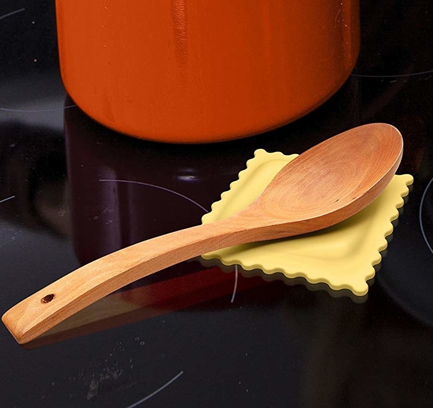 A wooden spoon sits on a spoon rest that looks like ravioli pasta. 
