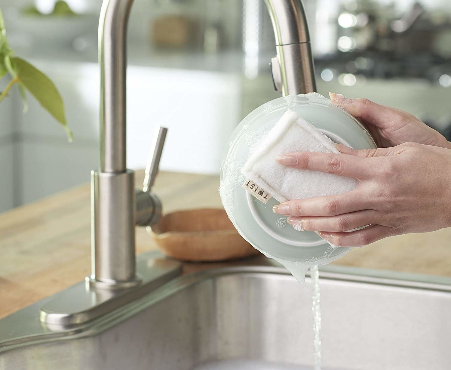 A sponge being held to a plate over the kitchen sink 