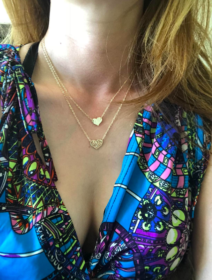 A reviewer wearing the gold necklace, which has a shorter chain with a smooth heart charm and longer chain with a textured heart charm