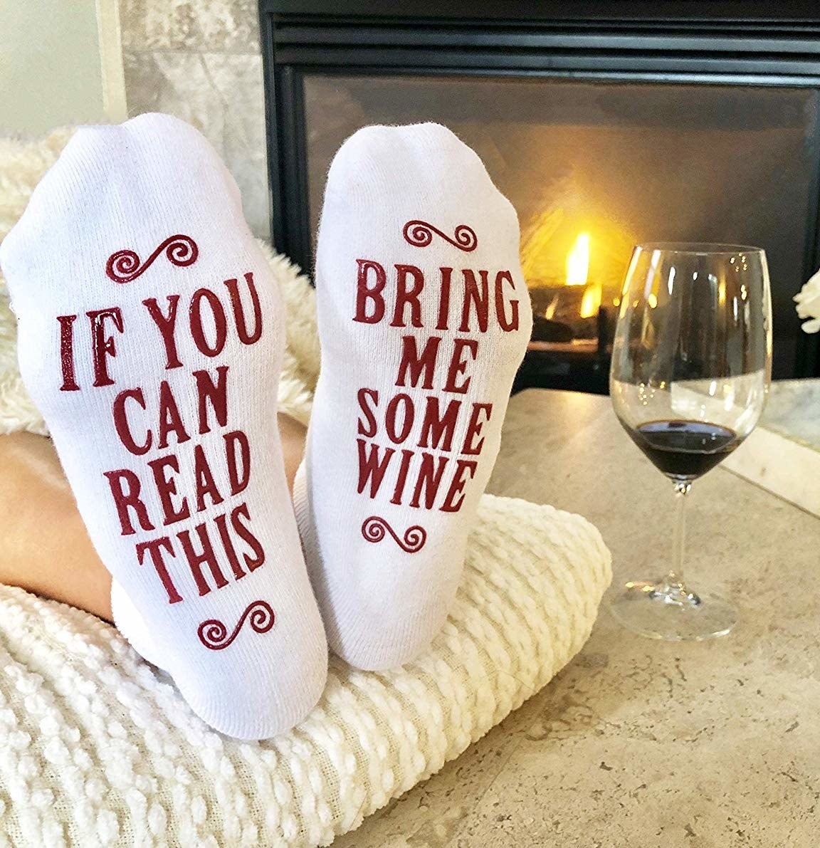 Person with feet up wearing socks that say on the sole "If you can read this bring me some wine"
