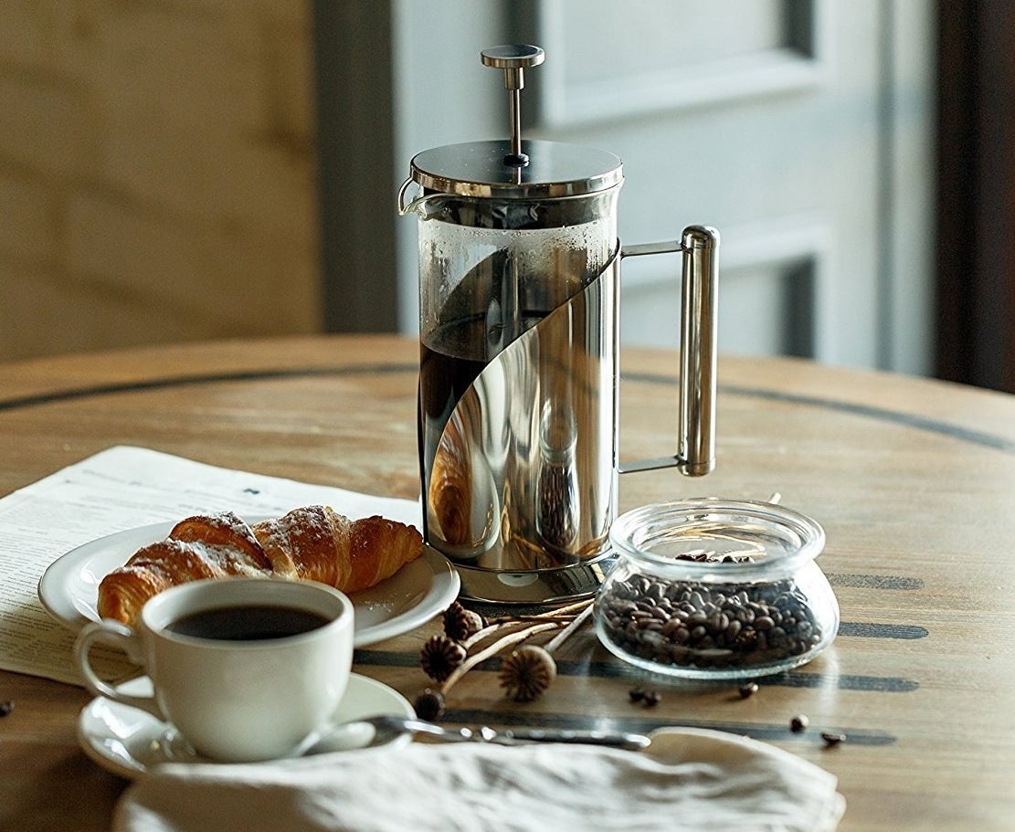 stainless steel french press next to plate with croissant