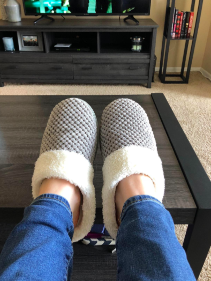 Reviewer&#x27;s feet wearing the grey fluffy slides. They&#x27;re closed-toe and have a line of fleece wrapping around the edge.