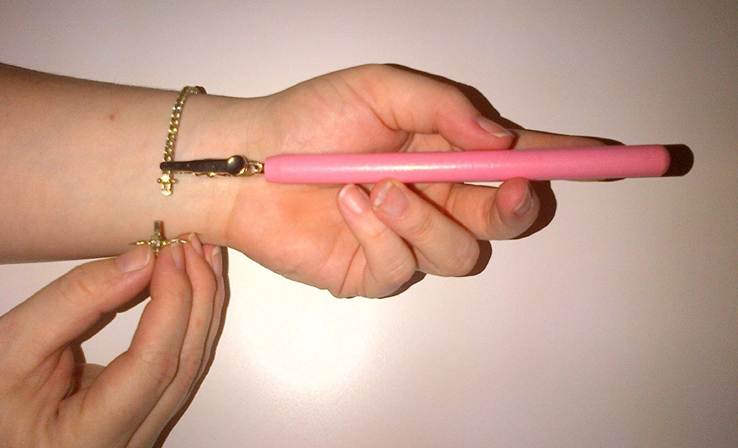 A hand holding a long-handled tool with a gripper to grip one end of a bracelet; a free hand to connects the clasp on the other end of the bracelet