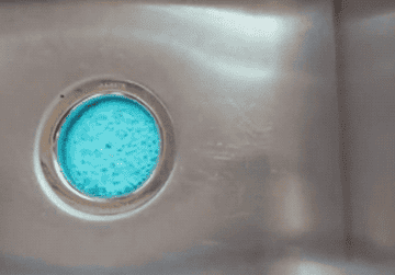 GIF close-up of a sink drain with a blue foam coming up out of the drain
