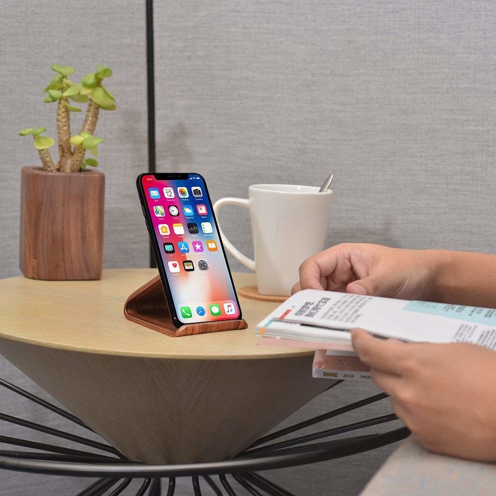 iPhone in phone dock on desk with coffee cup and person working