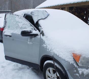 A car covered in snow with the cover on the windshield