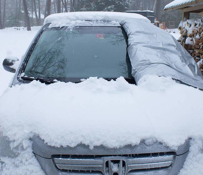A car covered in snow with the windshield cover partially taken off, showing how the windshield is snow-free
