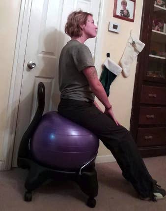 a reviewer sitting on a chair with the purple exercise ball as a seat