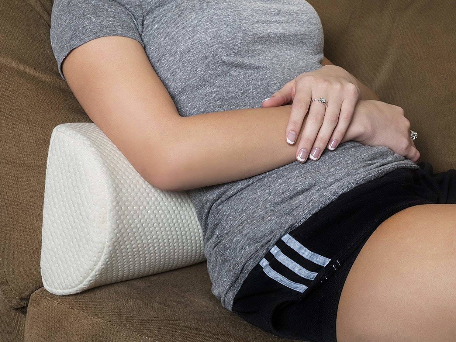 person sitting on a couch with long half-circular pillow used as a lumbar pillow