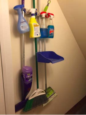reviewer's pic of wall mounted broom organizer with four cleaning tools and four cleaning spray bottles