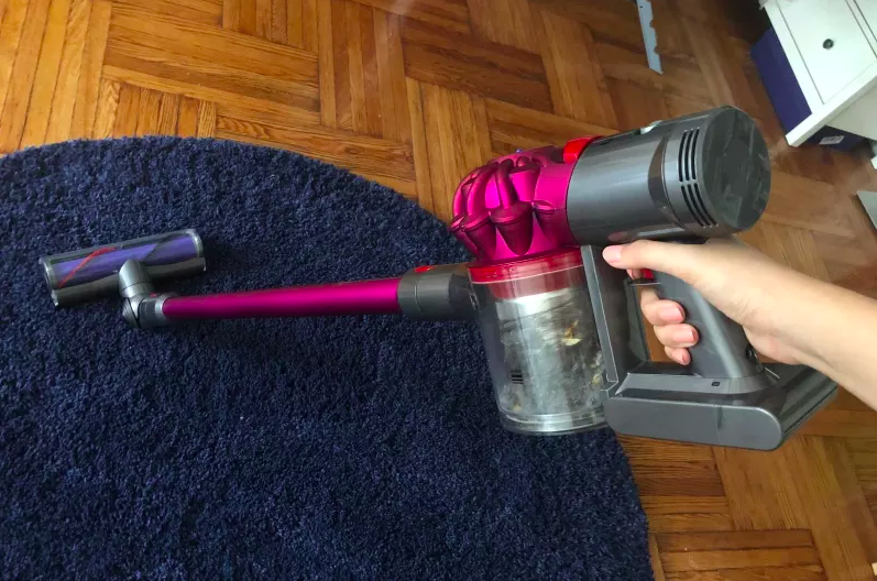 person using the stick vacuum on a rug