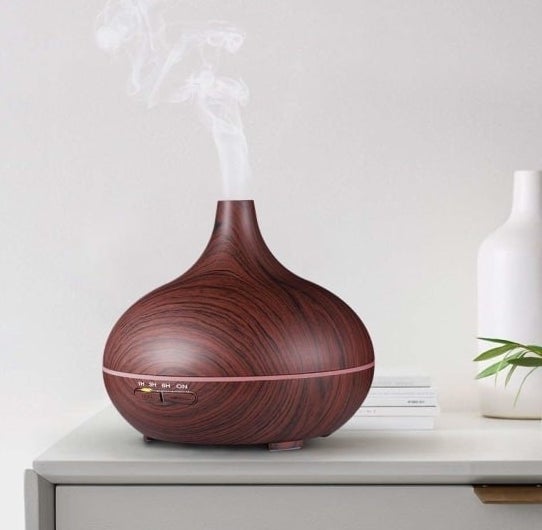 The diffuser in brown with a wood-like pattern sitting on a table releasing steam into the air